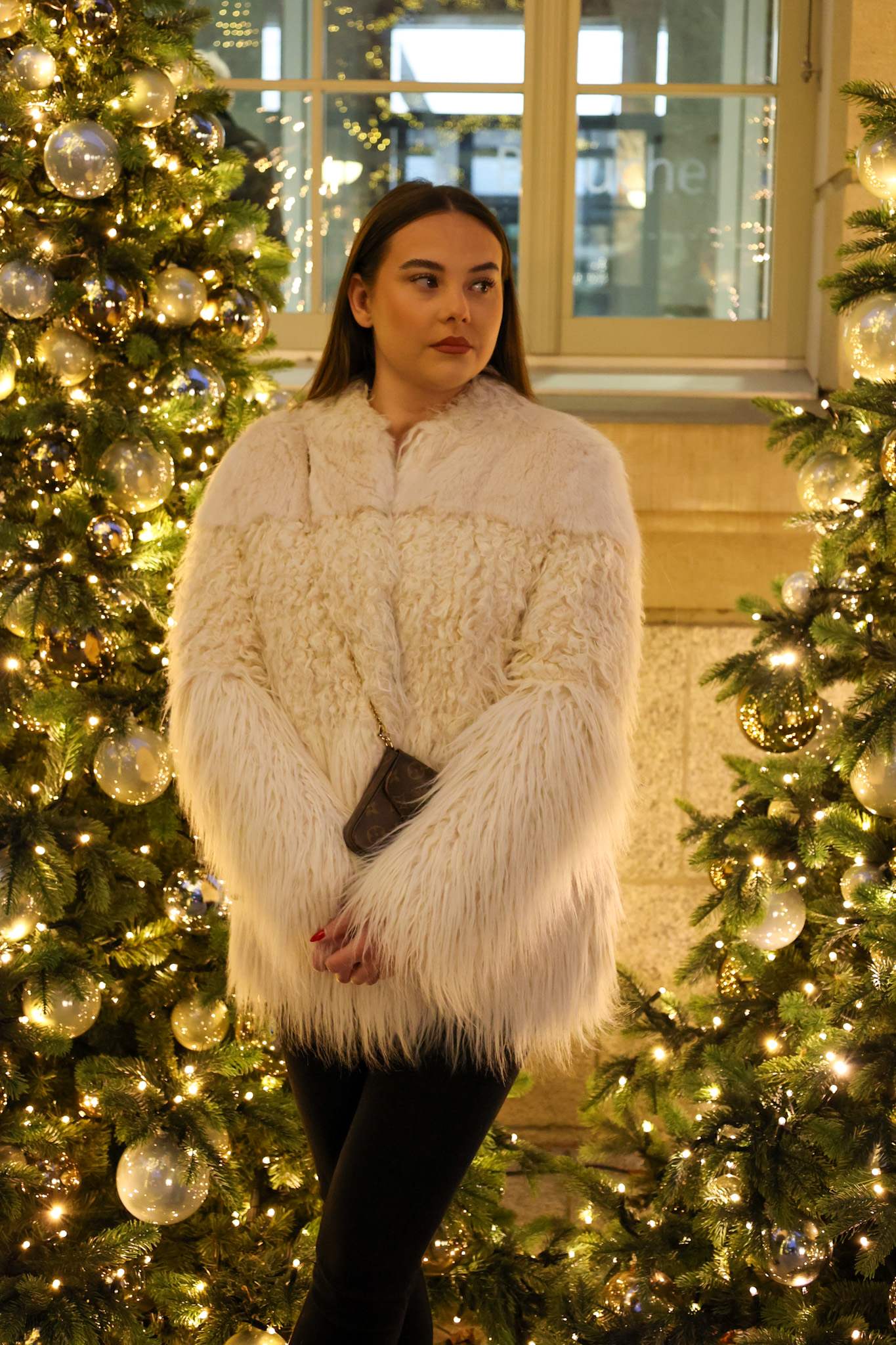 Frau in weißem Mantel vor Weihnachtsbäumen