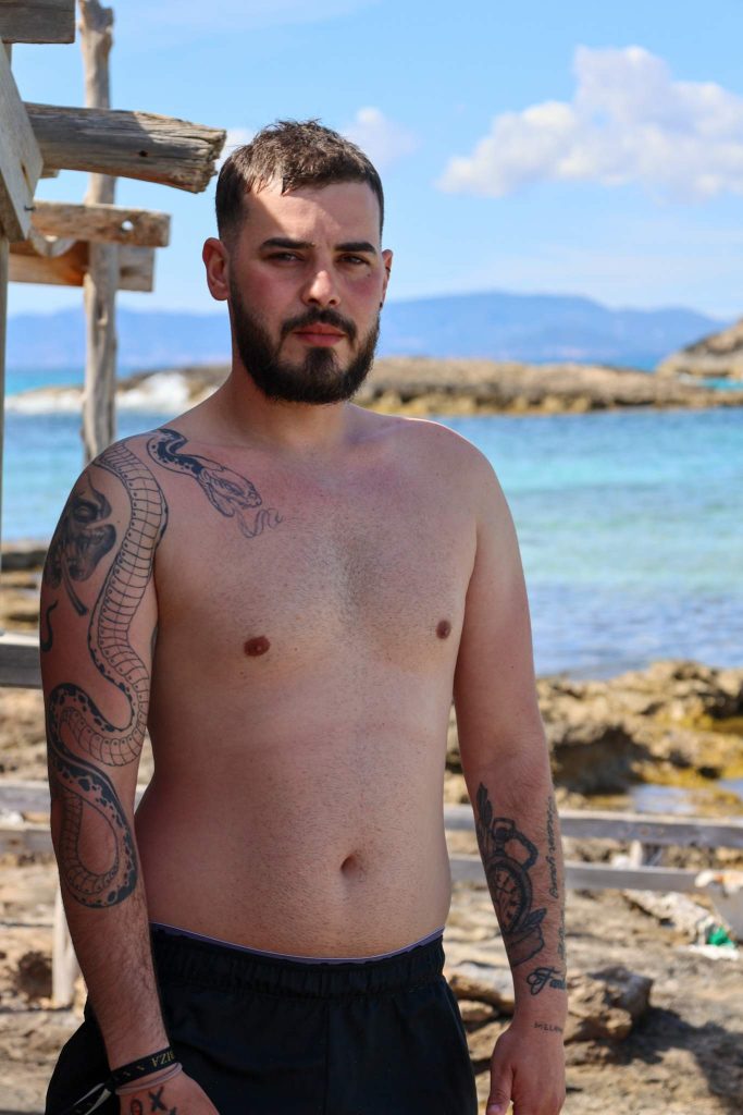 Mann oberkörperfrei mit Tattoos an Strand